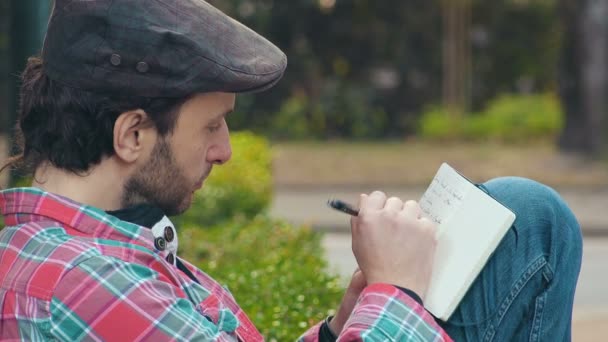 Jovem escritor escreve no diário no parque — Vídeo de Stock