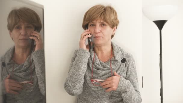 Olgun sarışın kadın evde telefonla konuşurken gülümseyen — Stok video