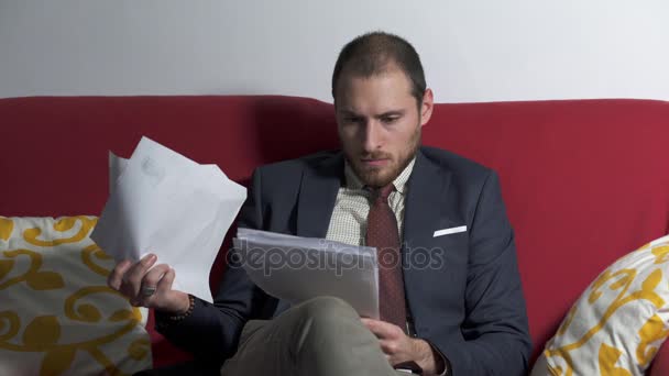 Nervous businessman on the couch checks the documents and starts throwing them — Stock Video