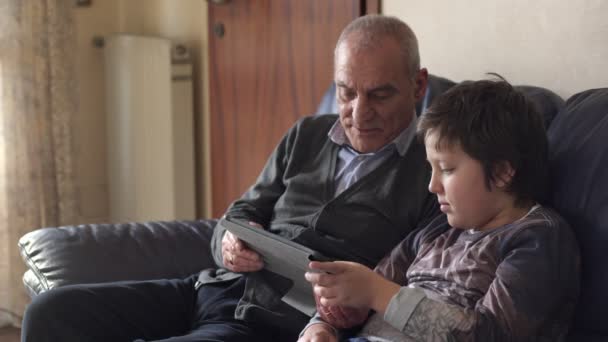 Family portrait: grandfather and grandson on the couch use the tablet — Stock Video