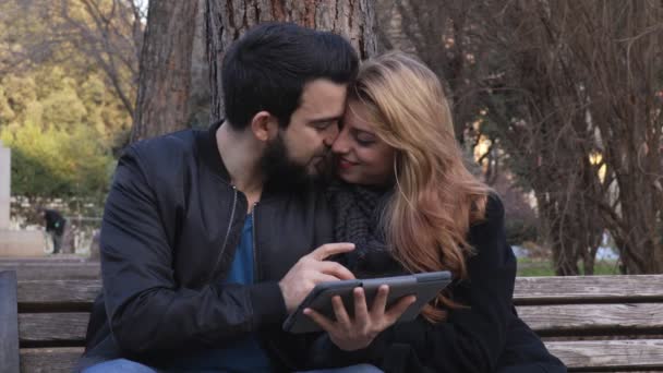 Gyönyörű pár a padra, nézni tabletta és csók — Stock videók