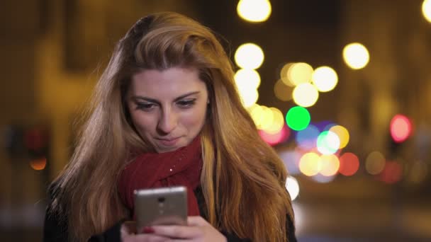夜市では、笑みを浮かべてスマート フォンで入力する金髪の女性の肖像画 — ストック動画