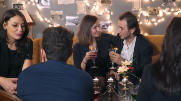 Las personas elegantes alrededor de la mesa hablan entre sí bebiendo bebidas — Vídeo de stock