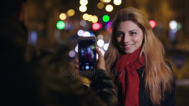 Улыбающаяся молодая женщина, пока ее парень фотографирует ее со смартфоном — стоковое видео