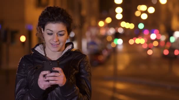 Улыбающаяся и счастливая женщина, пишущая смс на смартфоне, фон городских ночей — стоковое видео