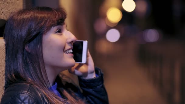 Jonge vrouw, leunend op een muur praten aan de telefoon in de straat in de nacht — Stockvideo