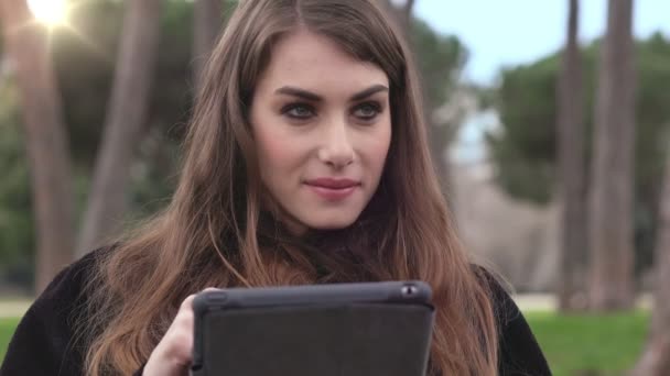 Симпатичная и красивая девушка пользуется табличкой в парке — стоковое видео