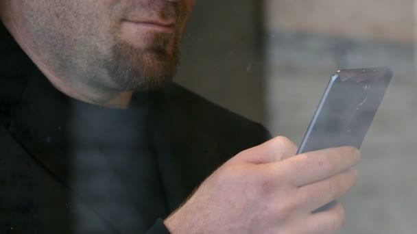 Detailní záběr na vousatý muž psaní na smartphone za skleněné okno — Stock video