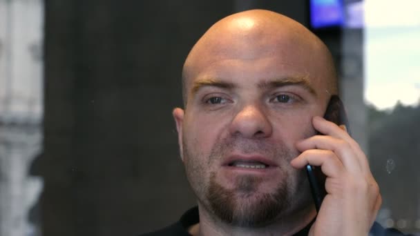 Σοβαρά φαλακρός άνδρας μιλάει στο τηλέφωνο πίσω από το τζάμι — Αρχείο Βίντεο