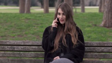 gülümseyen güzel kadın telefonda konuşurken bir parkta bankta oturan
