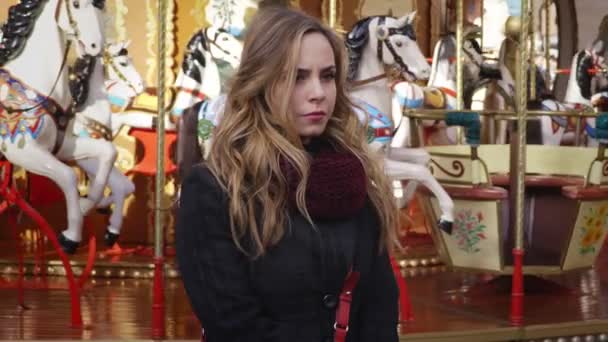 Worried  sad young blonde  woman waiting for someone, carousel runs background — Stock Video