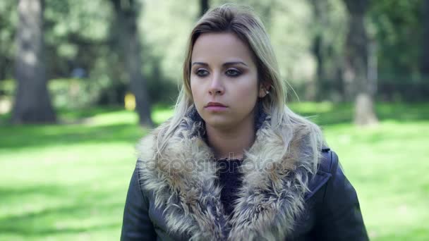 Szomorú töprengő fiatal szőke nő egyedül egy parkban portréja — Stock videók