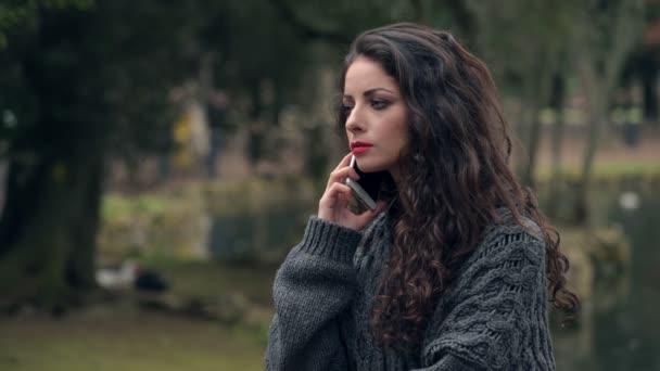 Nerveus boos brunette praten door de telefoon staande in park — Stockvideo