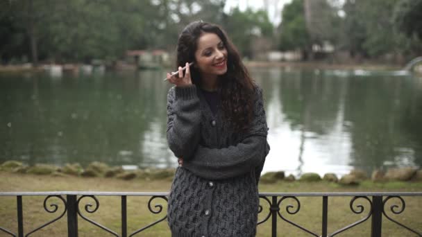 Relajada joven sonriente en el parque escuchando un mensaje de voz en el teléfono — Vídeos de Stock