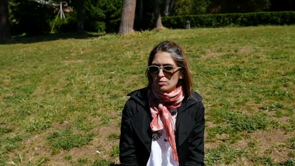 Niedliche junge Frau sitzt auf dem Gras sieht etwas -stetige Kamera — Stockvideo