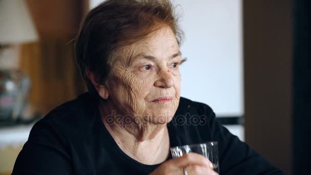 Stara kobieta sama w domu pije szklankę wody — Wideo stockowe