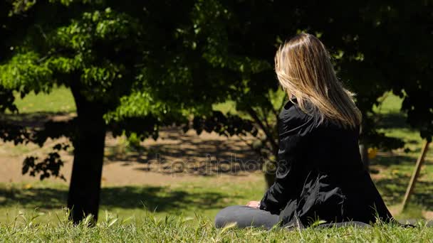 Ontspannen en meditatieve blonde vrouw zittend op het gras in stadspark — Stockvideo