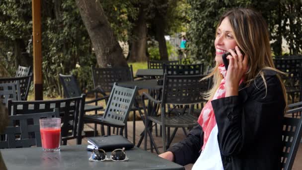 バー - 屋外に座ってスマート フォンで話して美しい幸せな女 — ストック動画