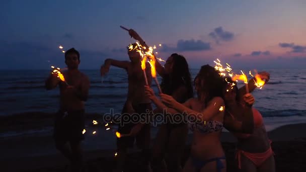 Gruppe von Freunden zündet gemeinsam Wunderkerzen am Strand bei Sonnenuntergang an — Stockvideo