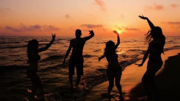 Silhueta de quatro amigos dançando na praia do oceano ao pôr do sol — Vídeo de Stock