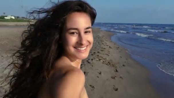 Камера следит за счастливой улыбчивой брюнеткой, бегущей по пляжу — стоковое видео