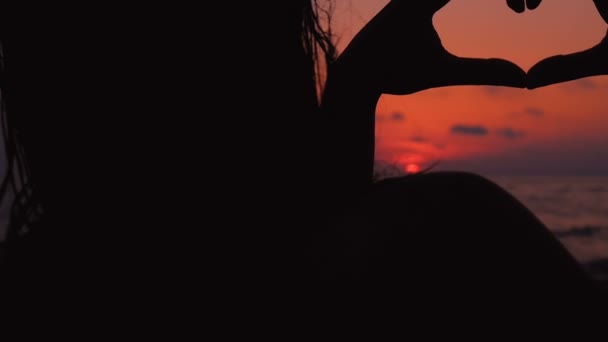 Kvinna händer att göra hjärtat mot solen på stranden under solnedgången — Stockvideo