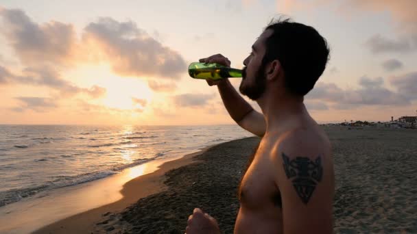 Розслаблений молодий чоловік споглядає захід сонця над морем в літній день — стокове відео