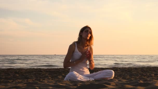 Mladá žena na pláži dělá jógu lotosové pozici při západu slunce — Stock video