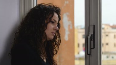 Üzgün ve dalgın genç kadın pencereden dışarı bakarak