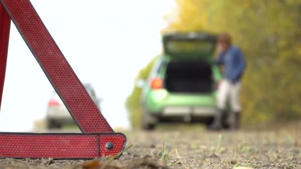 壊れた車の復旧サービスに緊急呼び出しを行う女性。国の道路で三角形の警告 — ストック動画