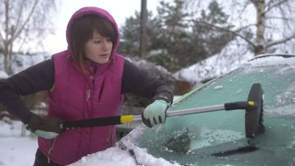 Jovem mulher limpando neve e gelo de seu carro. Inverno tempestade de neve — Vídeo de Stock