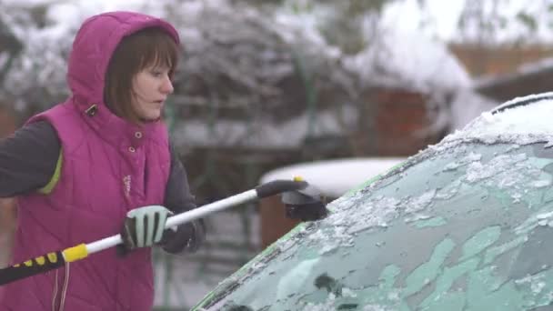 Giovane donna che pulisce neve e ghiaccio dalla sua auto. Tempesta di neve invernale — Video Stock