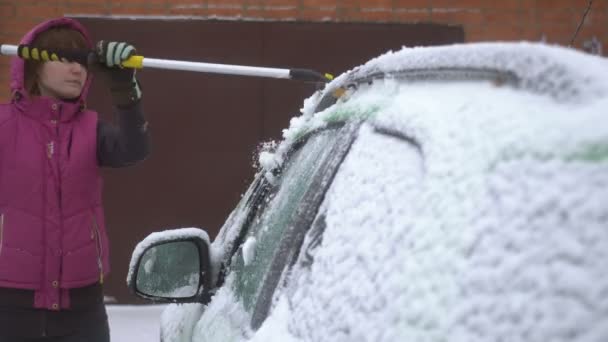 Mujer joven limpiando nieve y hielo de su coche. Tormenta de nieve — Vídeos de Stock