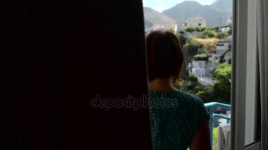 Kızıl saçlı kız otel ve mavi denize bakarak bir balkona açılır