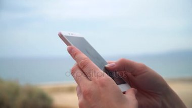 Kentin sahilinde oturan smartphone kullanarak elbiseli genç güzel kadın.