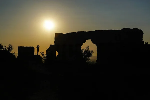 woman in a backlit ruins with the sun over the horizon
