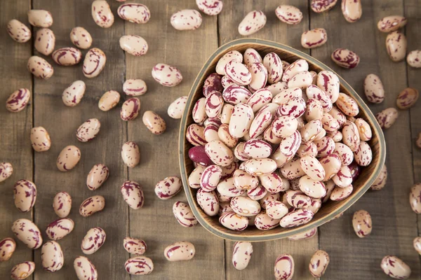 Raw pinto beans in bowl on wooden table