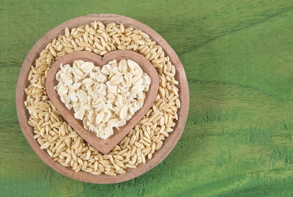 Semillas y copos de avena en forma de cuenco de madera corazón — Foto de Stock