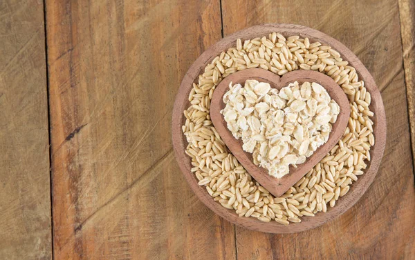 Semillas y copos de avena en forma de cuenco de madera corazón — Foto de Stock