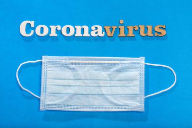 Korunaklı maskeli mavi arkaplan üzerindeki Coronavirus söz metni.