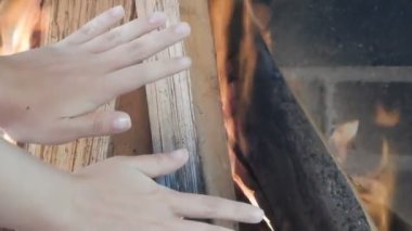 Eller şöminenin ateşini ısıtır.