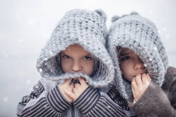 Девушка в вязаной серой шляпе обнимает своего замороженного младшего брата — стоковое фото