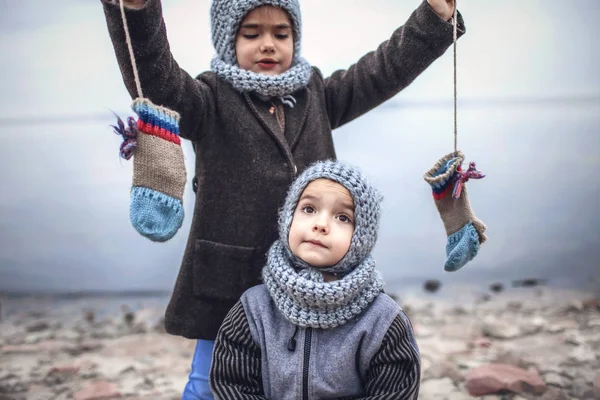 Девушка в вязаной серой шляпе делится перчатками со своим замороженным братом — стоковое фото
