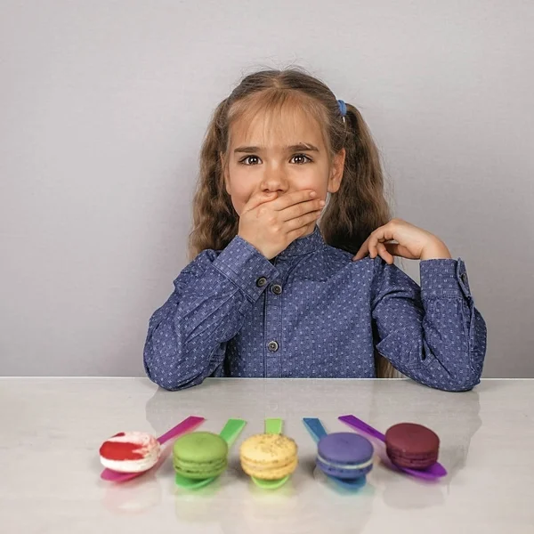 Linda niña estirando la mano a diferentes macarrones de colores , — Foto de Stock