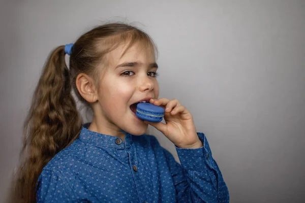 흰 백조 위 에서 파란색 마코 룬을 먹고 있는 귀엽고 작은 소녀 — 스톡 사진