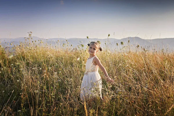 Cute girl dancing through a beautiful meadow with wheat and flow — Stock Photo, Image