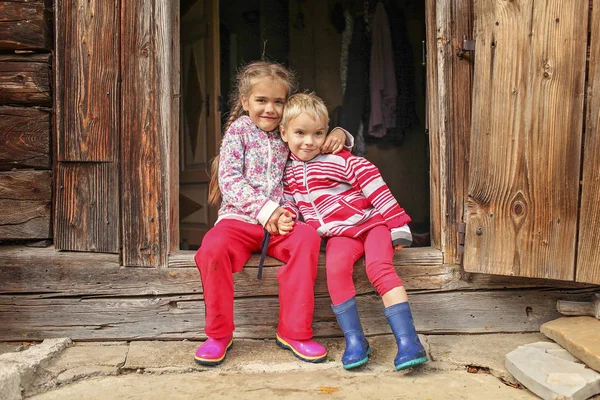 Children having rest on the doorstep of old wooden house during — Stock Photo, Image