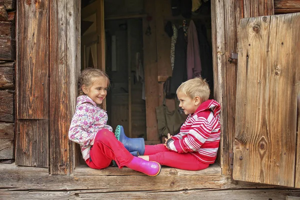 Children having rest on the doorstep of old wooden house during — Stock Photo, Image