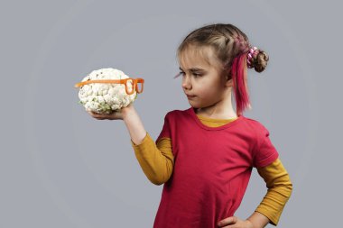 Ucube çocuğun elinde şekilsiz meyve ve sebzeler var., 