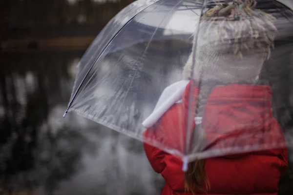 7-8 anni ragazza in cappotto rosso con ombrello trasparente a piedi alo — Foto Stock